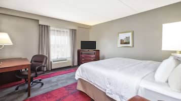 A hotel room with a bed, a desk, a chair, a TV, and a dresser.