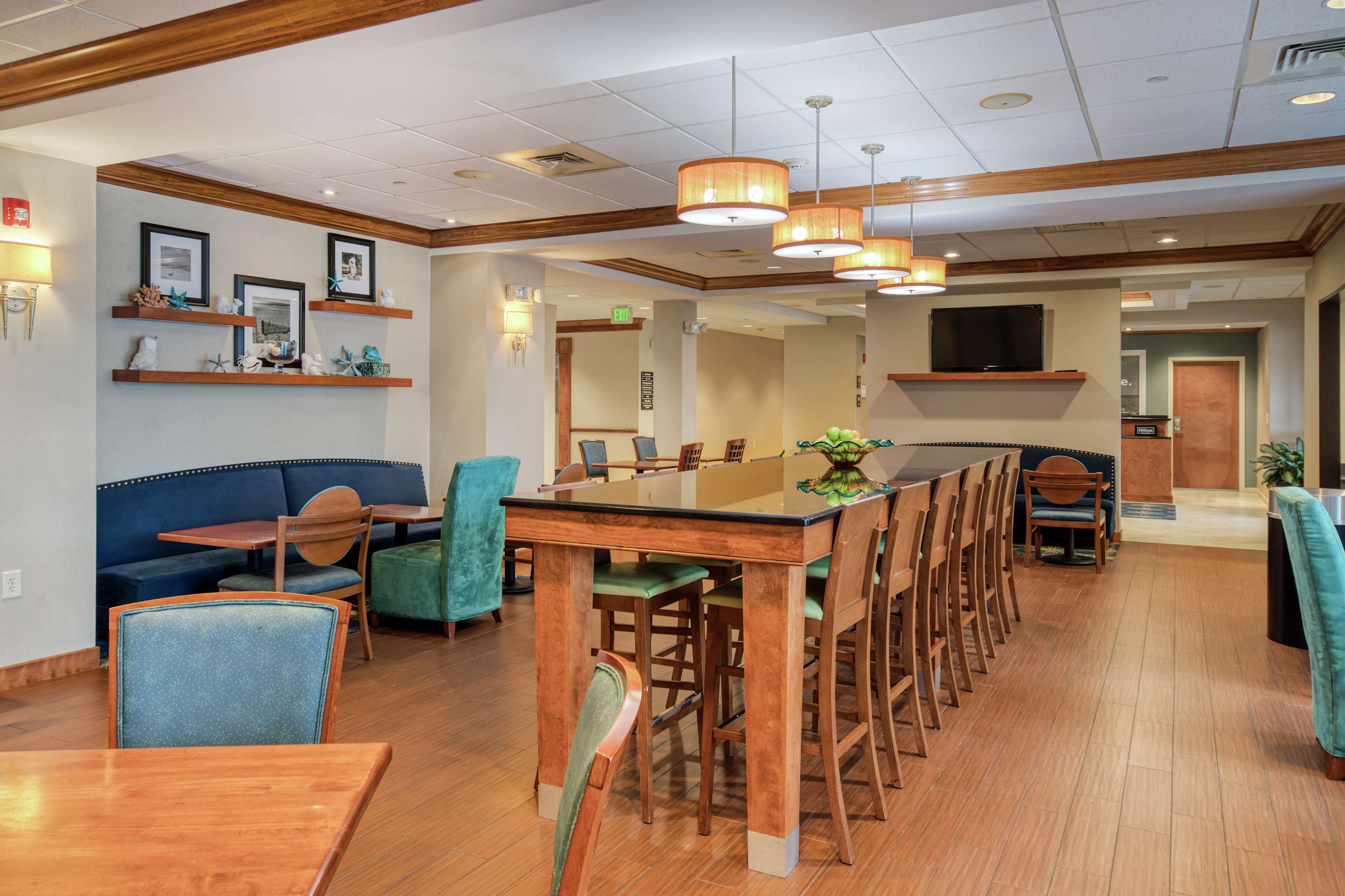 Un hall d’hôtel spacieux avec une longue table à manger en bois, plusieurs chaises, un canapé bleu et un téléviseur fixé au mur.