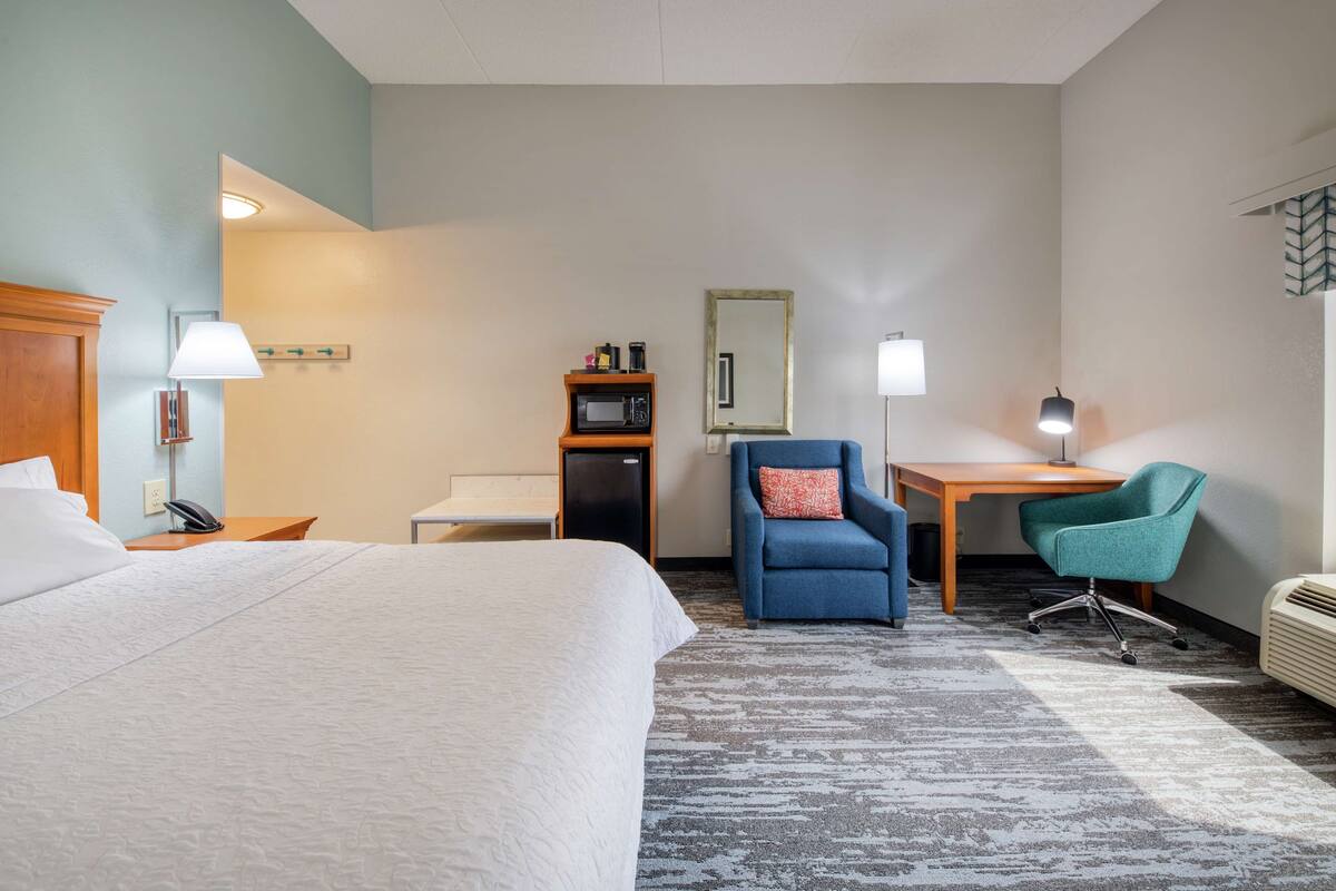 Ein Hotelzimmer mit Bett, Schreibtisch, zwei Stühlen, einer Mikrowelle, einer Lampe und einem Spiegel.