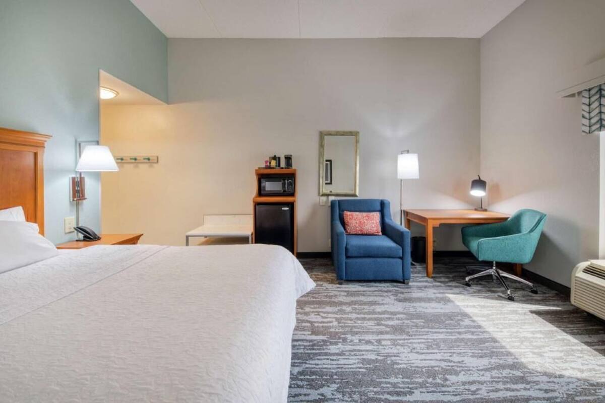 Ein Hotelzimmer mit Bett, Schreibtisch, zwei Stühlen, einer Mikrowelle, einer Lampe, einem Spiegel und einem Heizgerät.