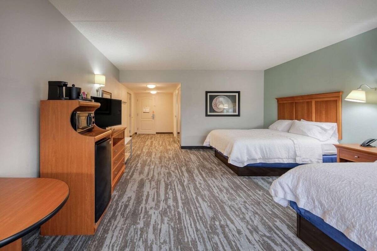 Ein Hotelzimmer mit Schreibtisch, zwei Betten, einem Fernseher und einem gerahmten Bild an der Wand.
