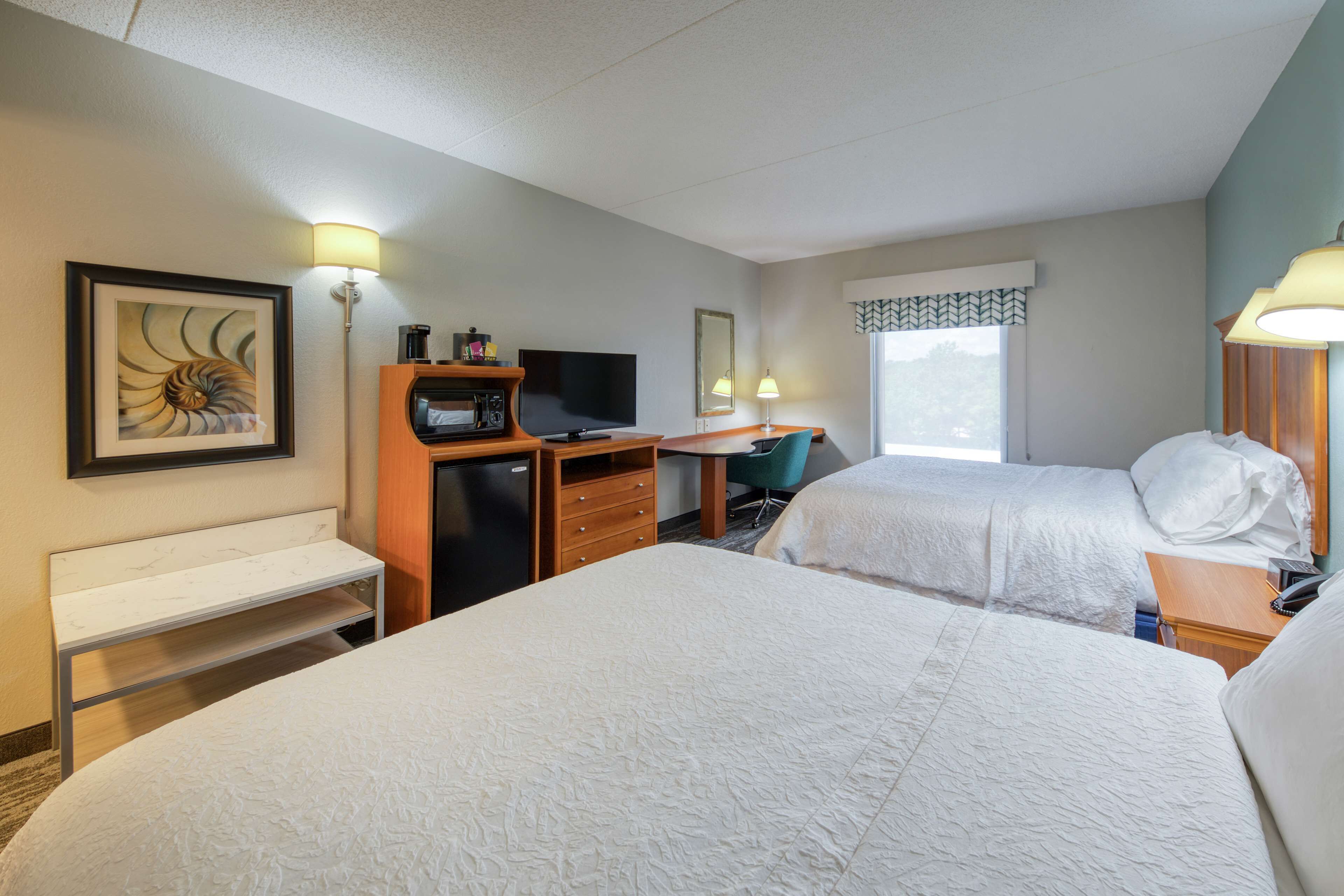 A hotel room with two beds, a desk with a computer, a TV, and a lamp.