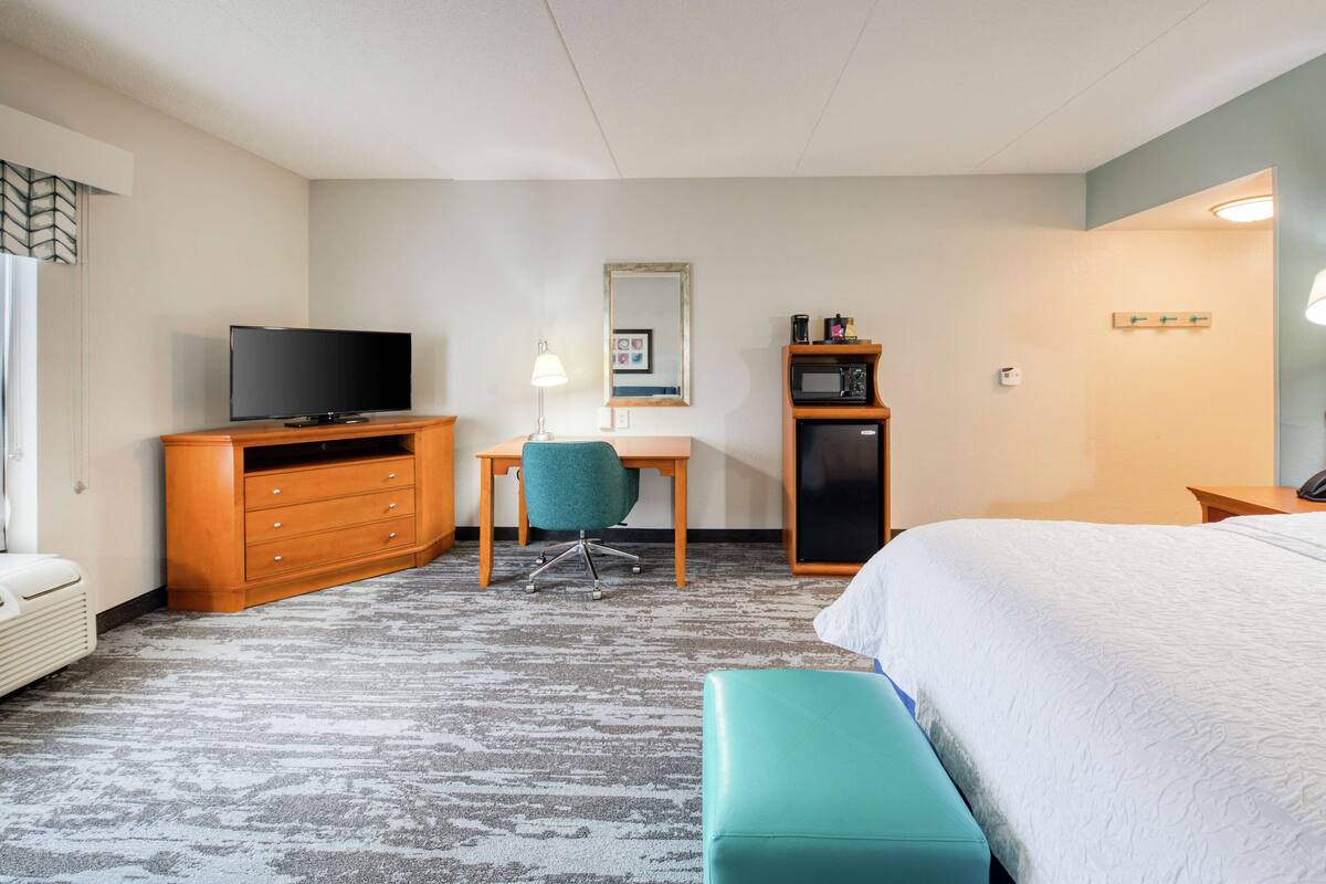 Ein Hotelzimmer mit einem Bett, einem Schreibtisch mit Stuhl, einem Fernseher, einer Mikrowelle und einem kleinen Schrank.