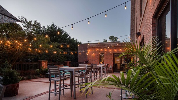 An outdoor patio with string lights, tables, and chairs. - Hampton Inn Wilmington - University Area/Smith Creek Station (Wilmington)