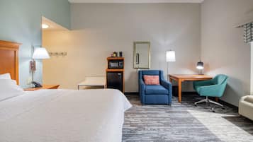 A hotel room with a large bed, a desk, two chairs, a microwave, a telephone, and a mirror.