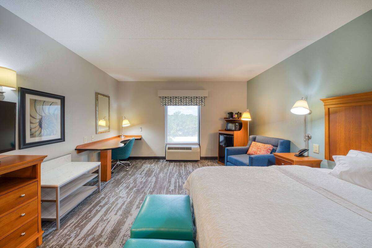 Ein Hotelzimmer mit Bett, Schreibtisch, Stuhl, Mikrowelle und Fenster.