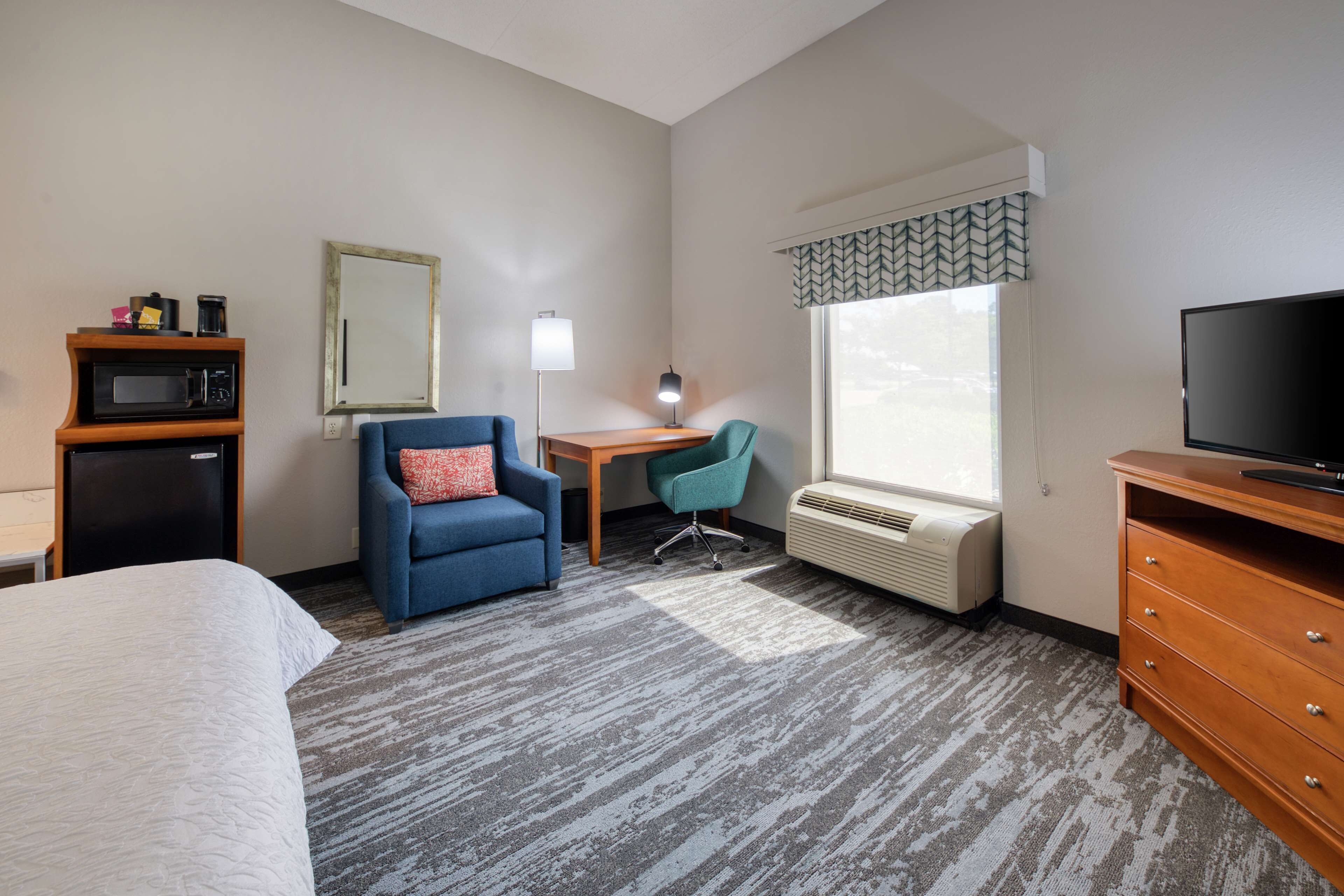 Habitación de hotel con cama, escritorio, silla, televisor, microondas y calefacción.