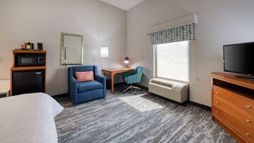 Habitación de hotel con cama, escritorio, silla, televisor, microondas y calefacción.