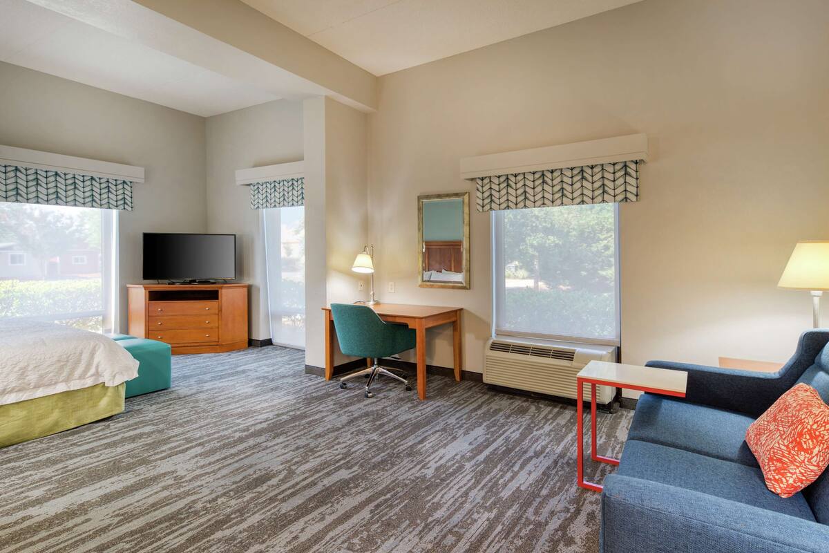 Ein Hotelzimmer mit Bett, Schreibtisch, Stuhl, Fernseher, Lampe und einer Couch.