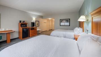 Una habitación de hotel con dos camas, un escritorio con microondas, un refrigerador pequeño y una lámpara.