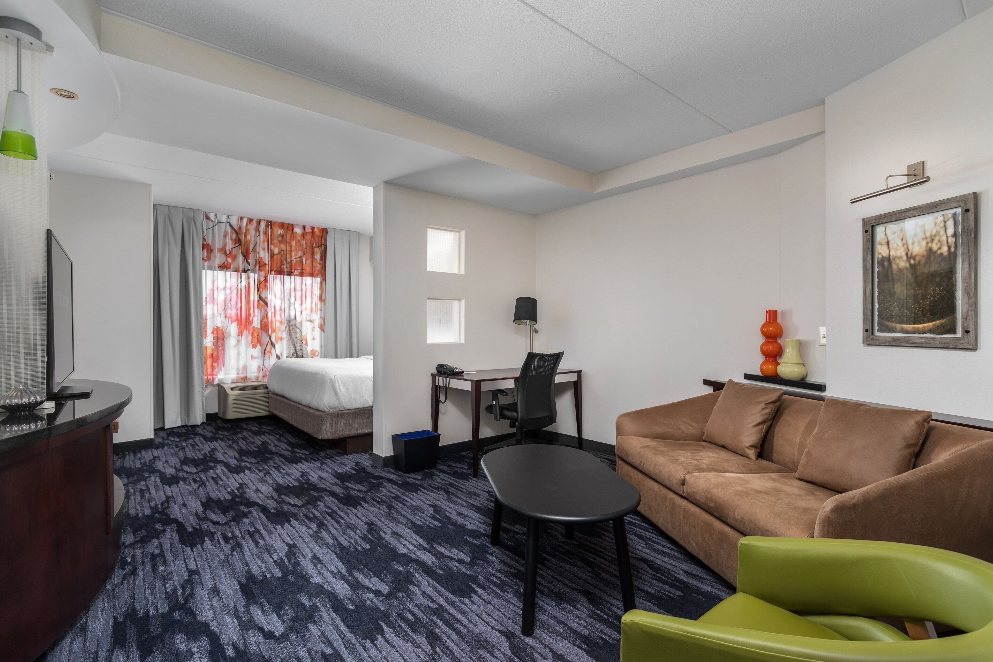 A hotel room with a bed, a desk with a chair, a sofa, and a television.