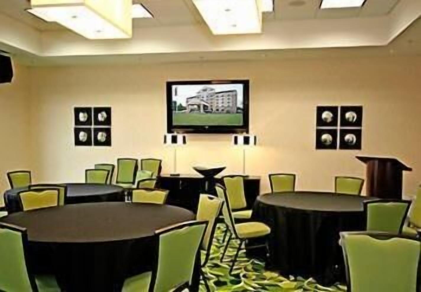 A conference room with a large table and chairs, a television mounted on the wall, and framed pictures on the walls.