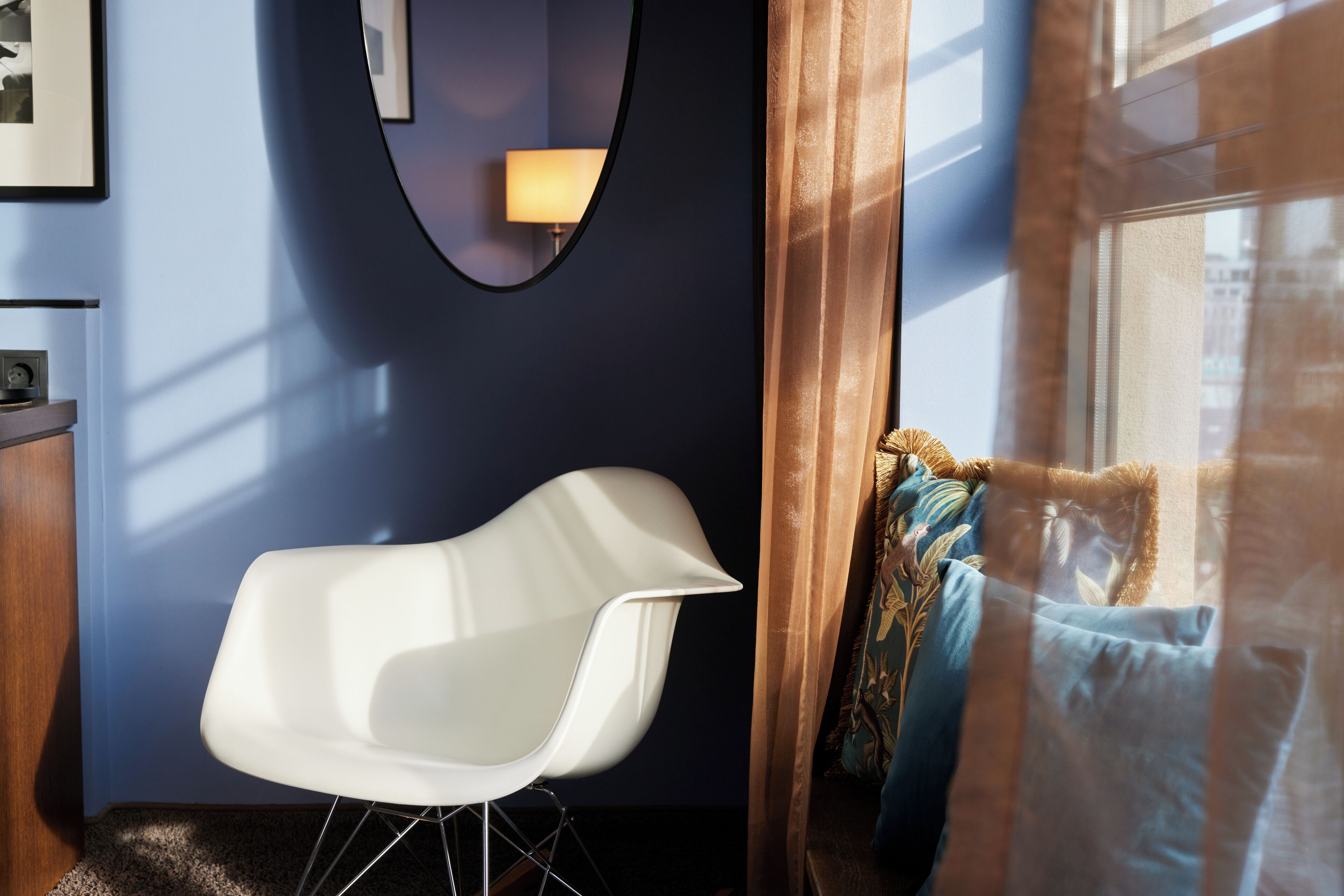 Una habitación moderna con una silla blanca, una pared azul oscuro y una ventana con cortinas.