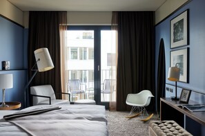 A hotel room with a bed, a desk, a chair, a rocking chair, and a balcony with chairs.