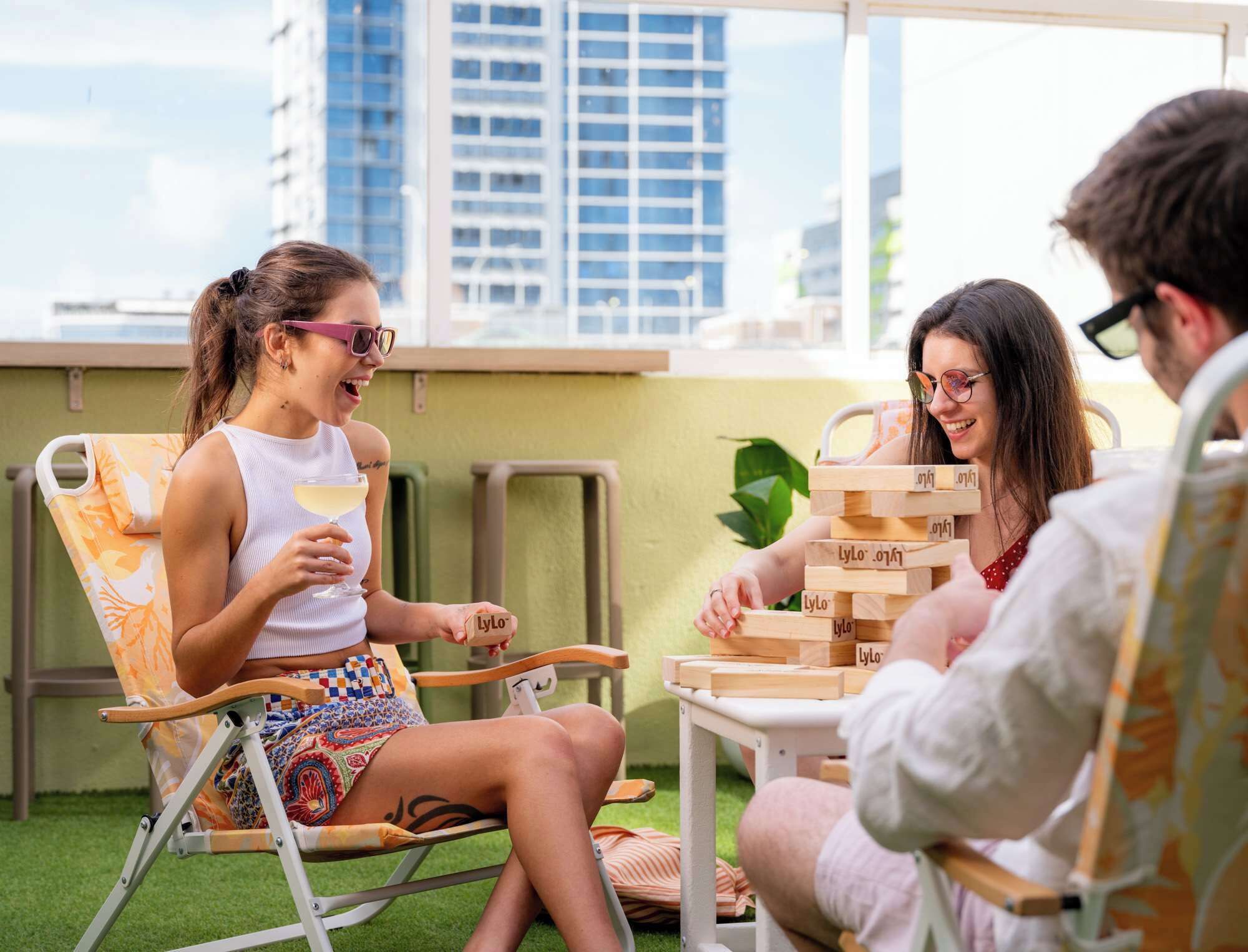 Un groupe de personnes jouant à un jeu de société sur une terrasse en toit, avec vue sur la ville.