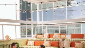 Amplia habitación con ventanas grandes, un sofá con cojines y tres personas ejercitándose en colchonetas.