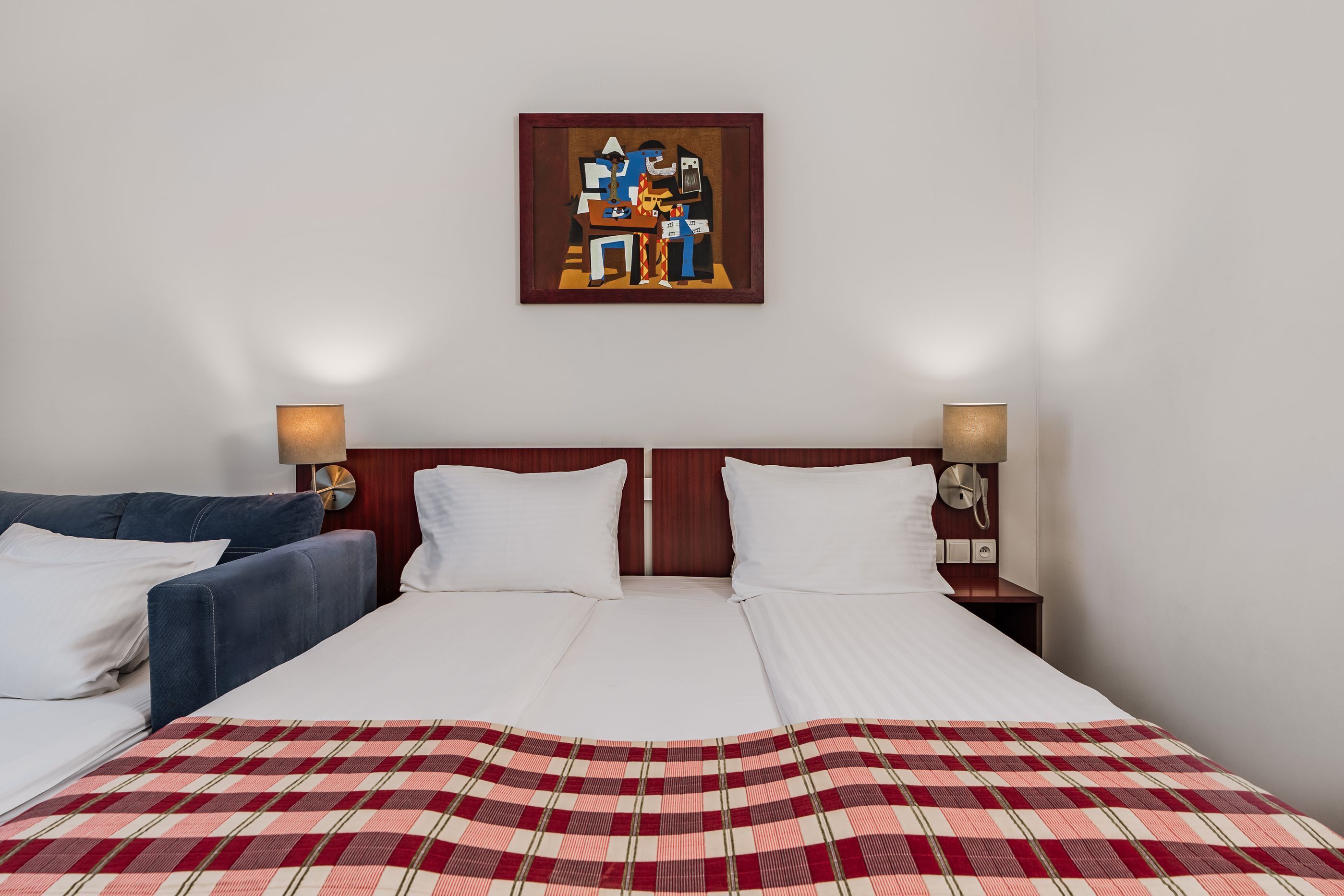 A hotel room with a large bed, two bedside tables with lamps, a blue sofa, and a painting on the wall.