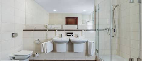 A modern bathroom with a toilet, bidet, two sinks, a shower, and a mirror.