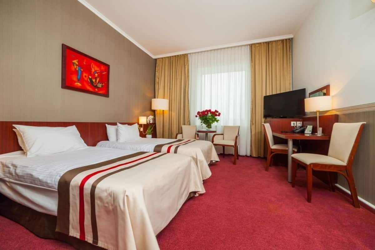 Une chambre d’hôtel avec deux lits, un bureau, une chaise, une télévision et un tableau au mur.