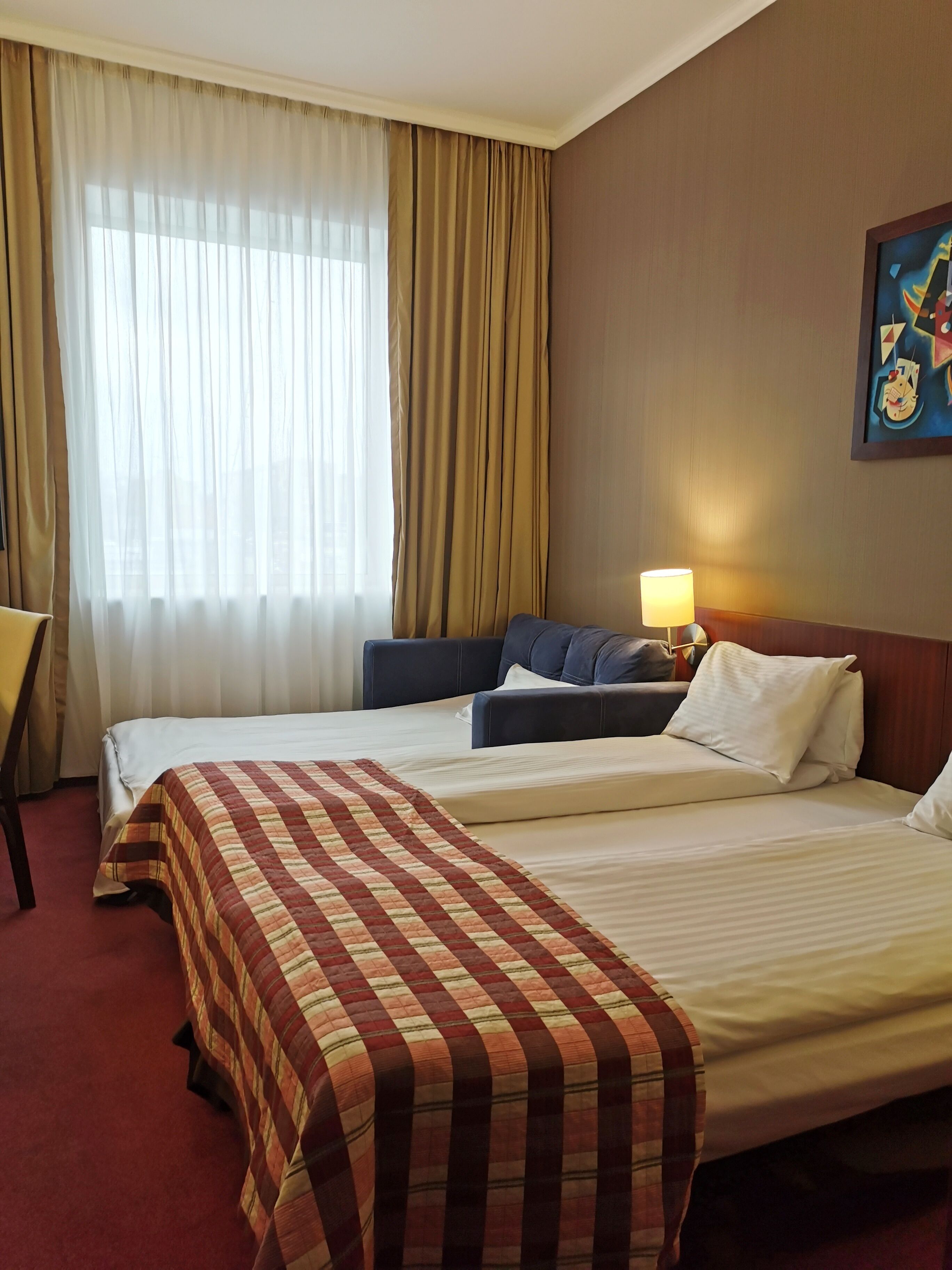A hotel room with two beds, a desk, a lamp, and a painting on the wall.