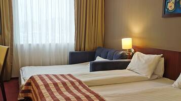 A hotel room with two beds, a desk, a lamp, and a painting on the wall.