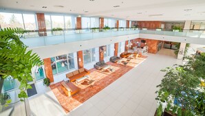 Een ruime, moderne atriumruimte met een hoge plafond, verschillende zithoeken en veel daglicht.