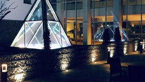 Een modern gebouw met een glazen gevel, een geometrische lichtinstallatie en een trap.