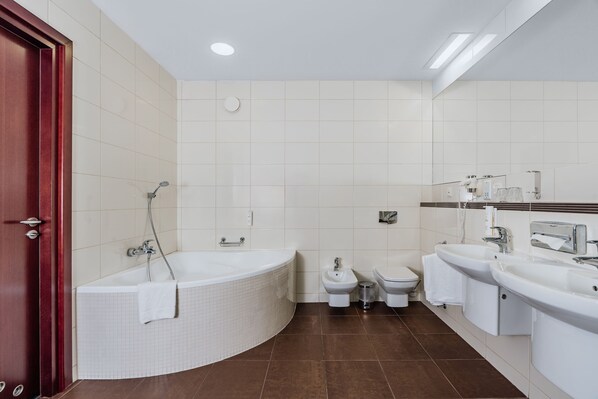 A modern bathroom with a bathtub, two toilets, and two sinks.