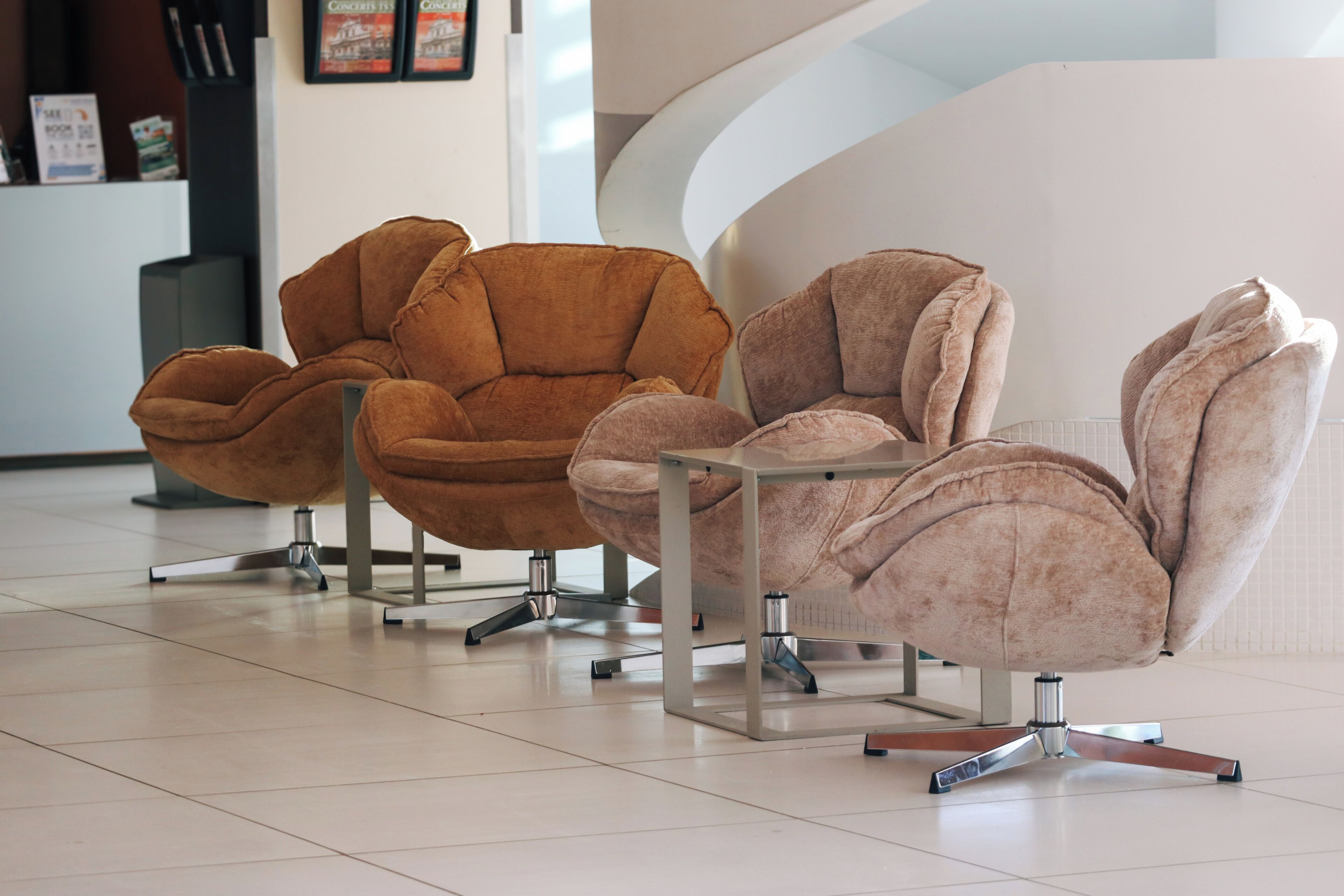 Three modern chairs with metal frames and swivel bases, arranged in a row on a tiled floor.