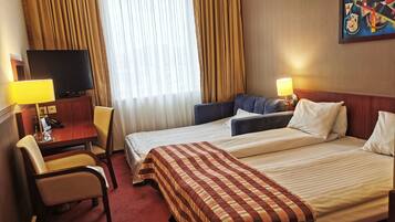 A hotel room with a bed, a desk with a lamp, a chair, a television, and a painting on the wall.