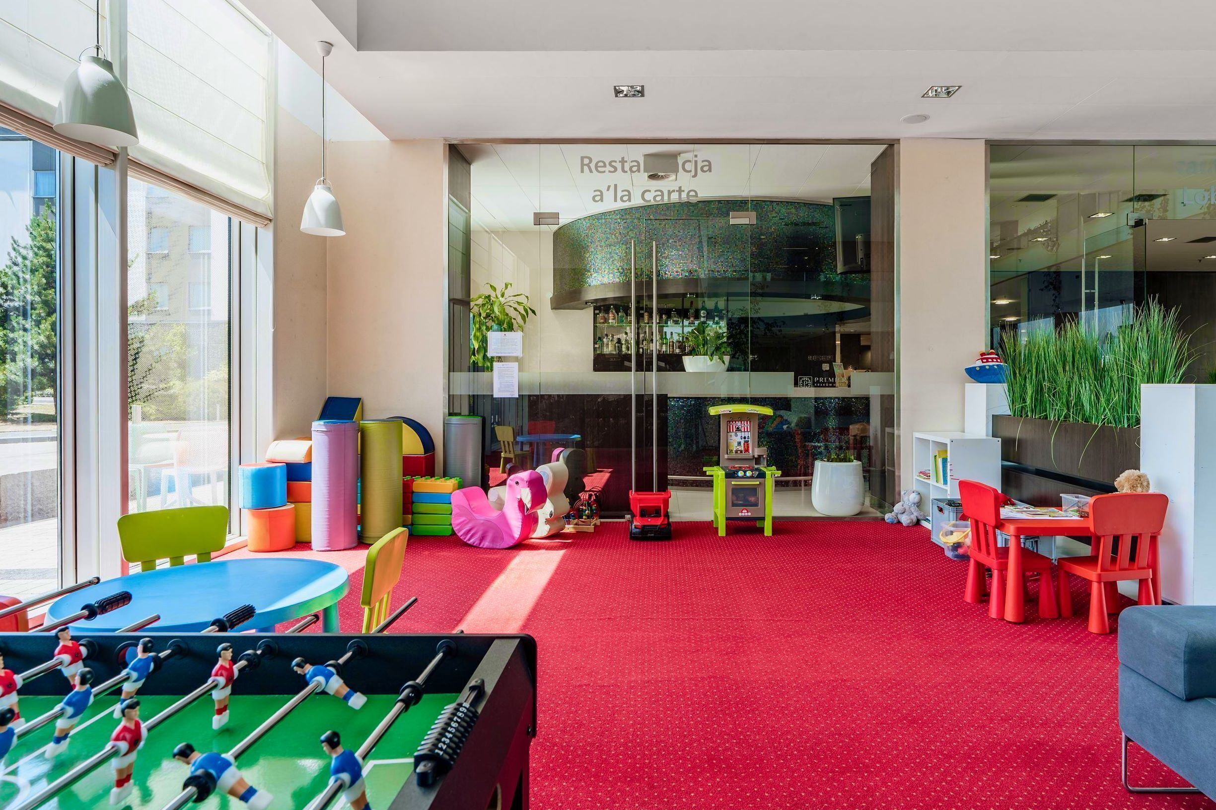 Zona de juegos infantiles con mesa de fútbol de mesa, asientos coloridos y una alfombra roja.
