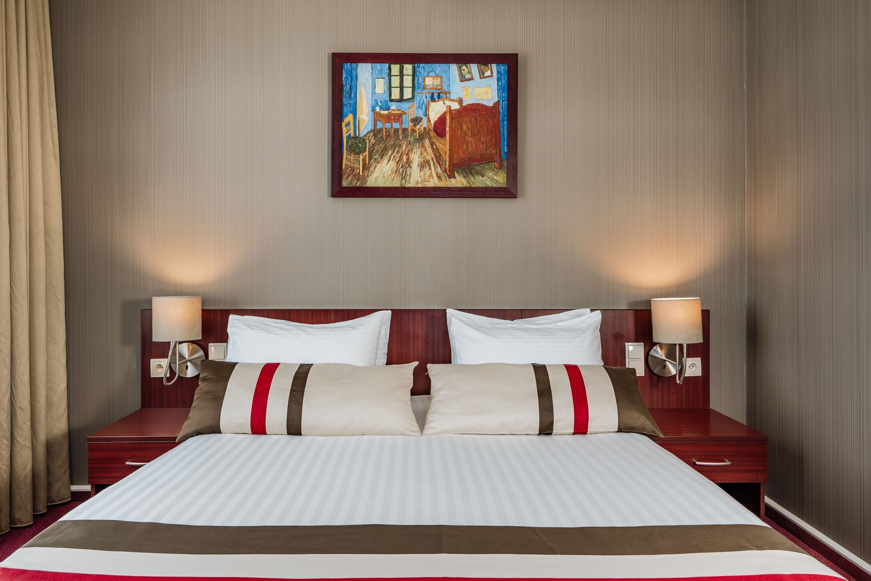 Une chambre d’hôtel avec un grand lit, deux tables de chevet avec des lampes, un tableau au mur et une tête de lit en bois.