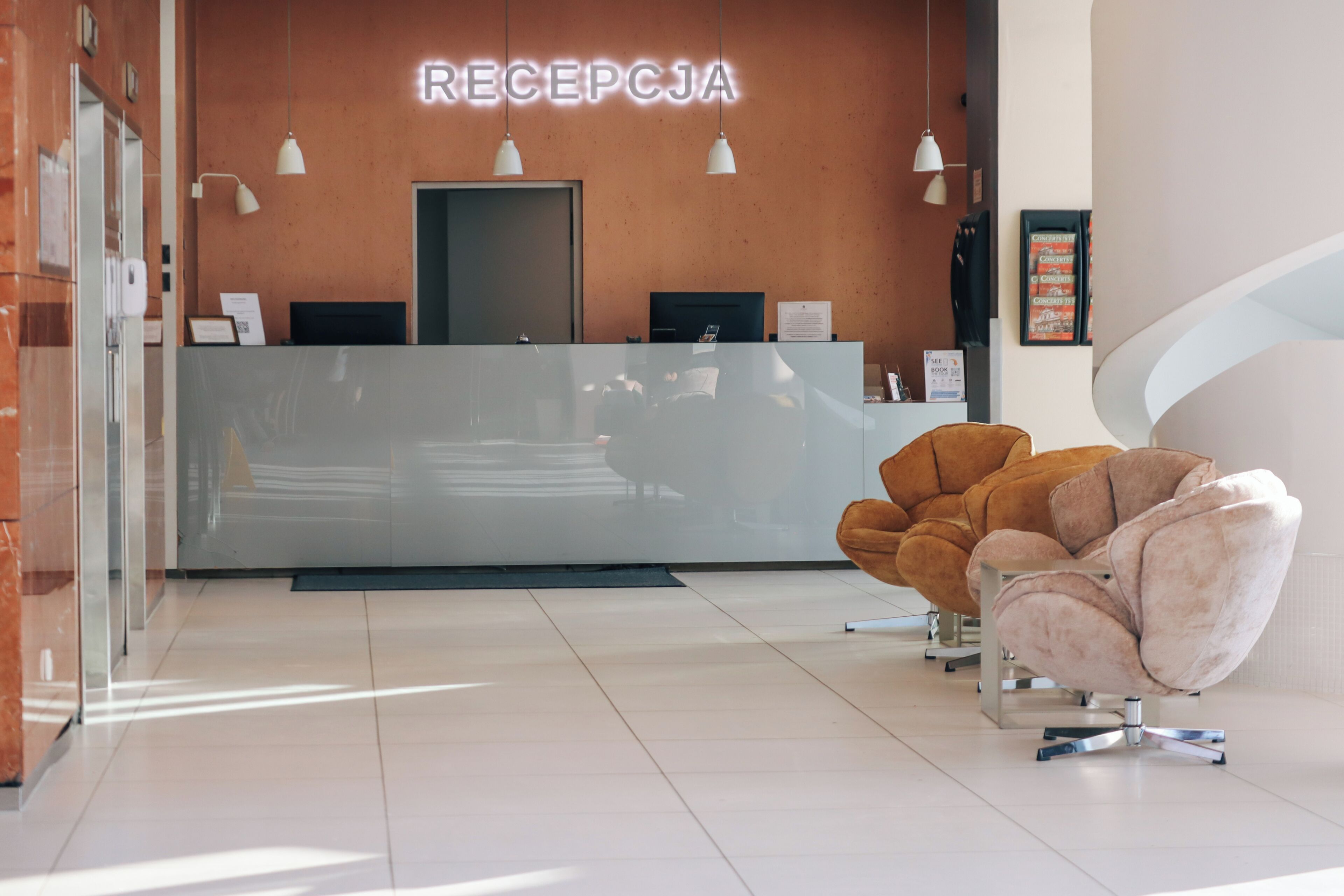 A reception area with a reception desk, two computer monitors, a brown chair, and a white chair.