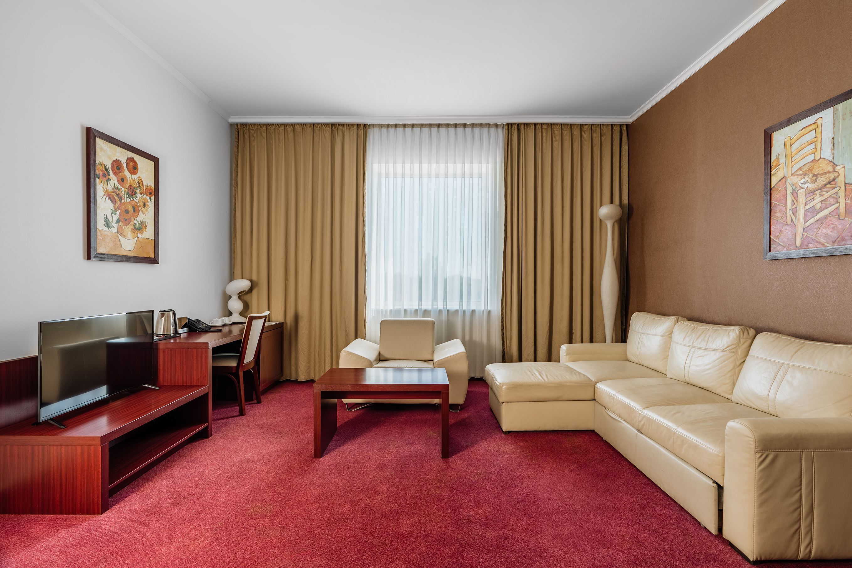 Habitación de hotel con televisor, sofá, sillón, mesita de centro y una ventana grande con cortinas.
