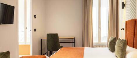 Een hotelkamer met een bed, een bureau, een stoel, een televisie en een raam met gordijnen.