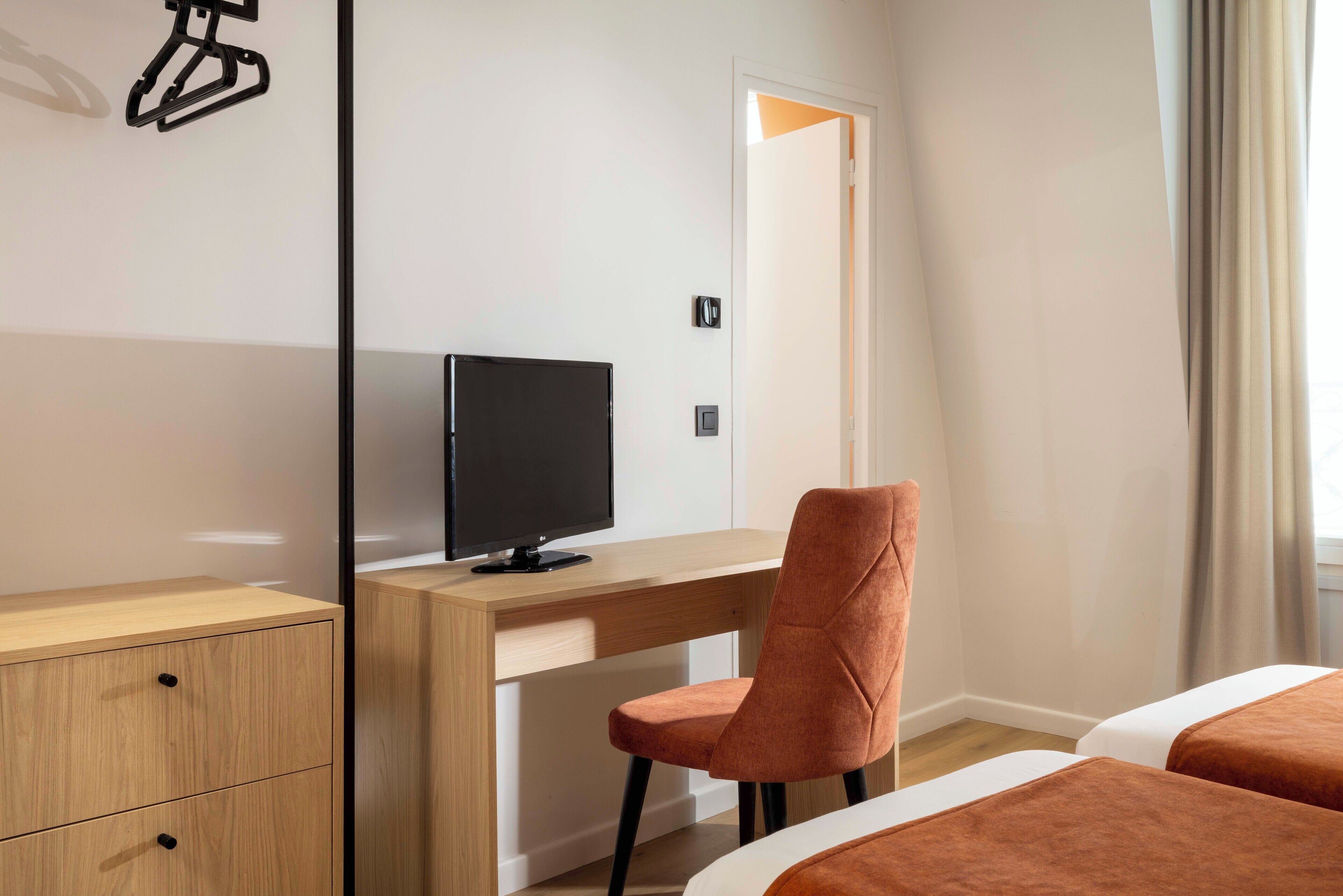 Ein Hotelzimmer mit einem Holztisch, einem Fernseher, einem Sessel und zwei Betten.