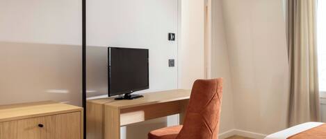 Ein Hotelzimmer mit einem Holztisch, einem Fernseher, einem Sessel und zwei Betten.
