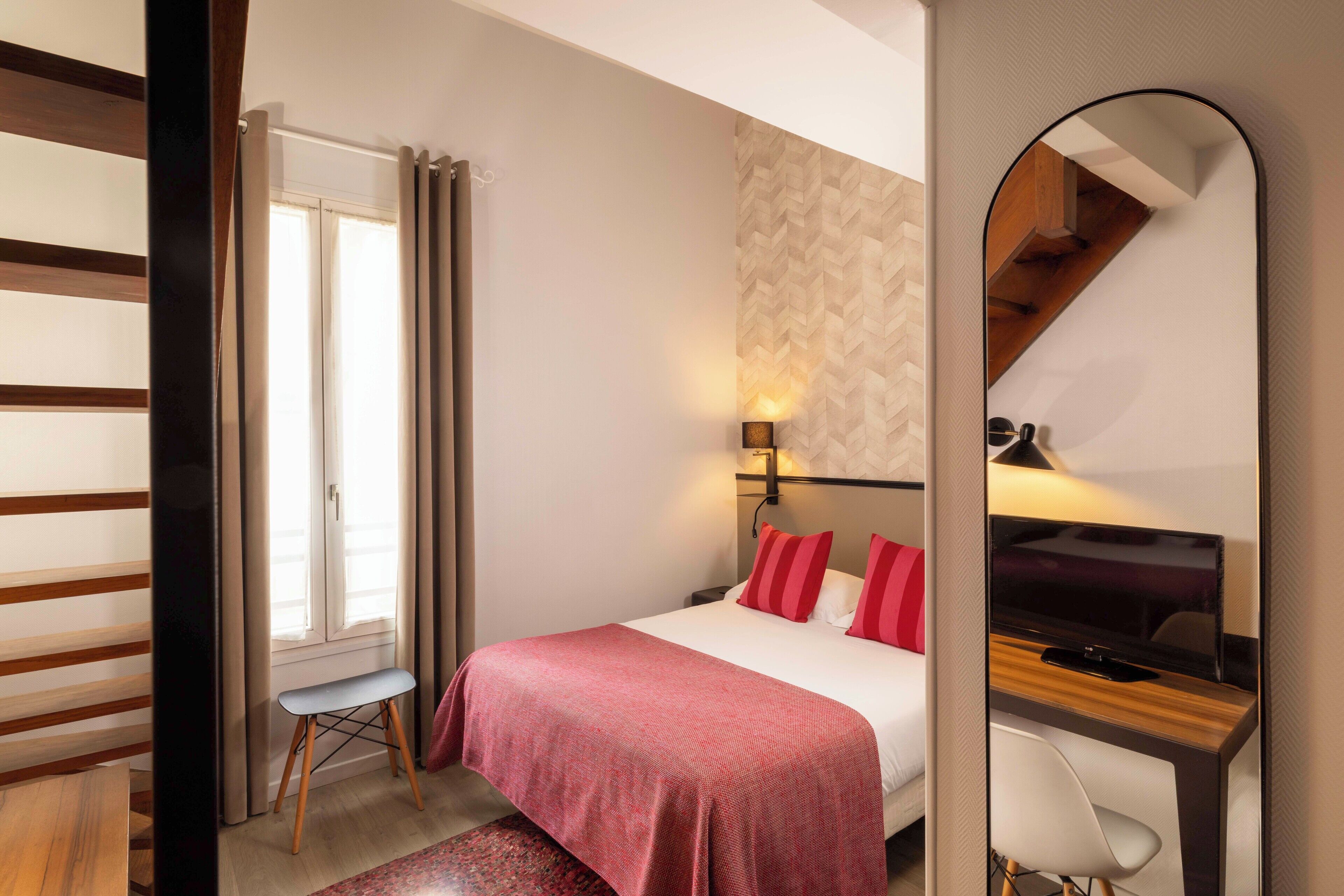 A bedroom with a bed, bedside table, lamp, and a mirror.