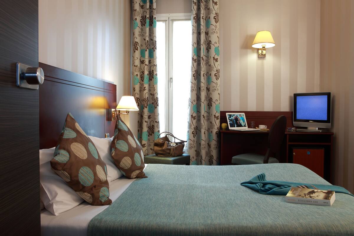 A hotel room with a bed, a desk, a television, and a lamp.