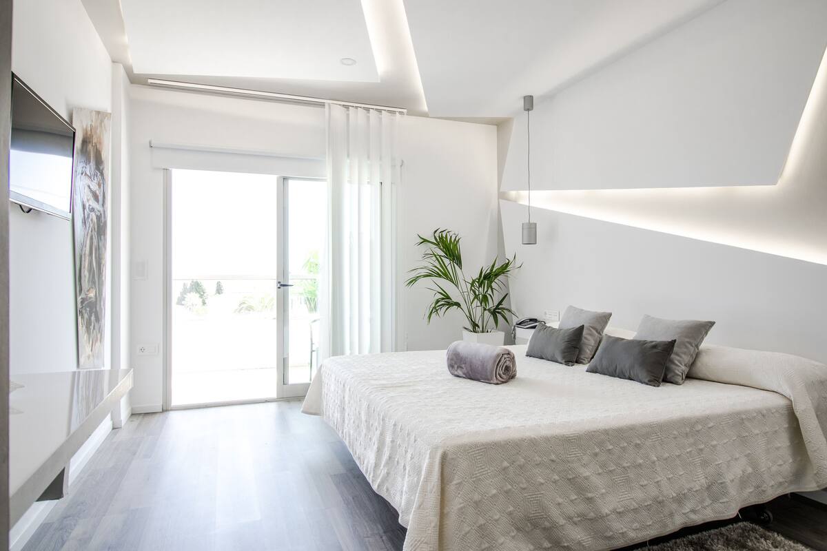 A modern bedroom with a large bed, a potted plant, and a sliding glass door leading to an outdoor area.