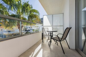 En balkong med ett bord och stolar, med utsikt över ett bostadsområde med palmer och hus.