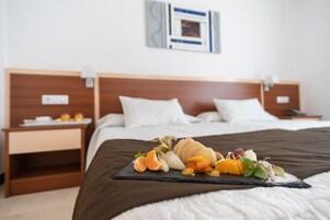 A neatly made bed with a fruit platter on the bedspread, a wooden headboard, and a nightstand with a small table.