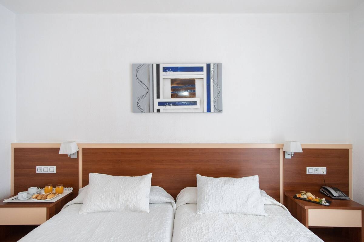 A hotel room with a double bed, two bedside tables, a wall-mounted artwork, and a nightstand with a lamp.