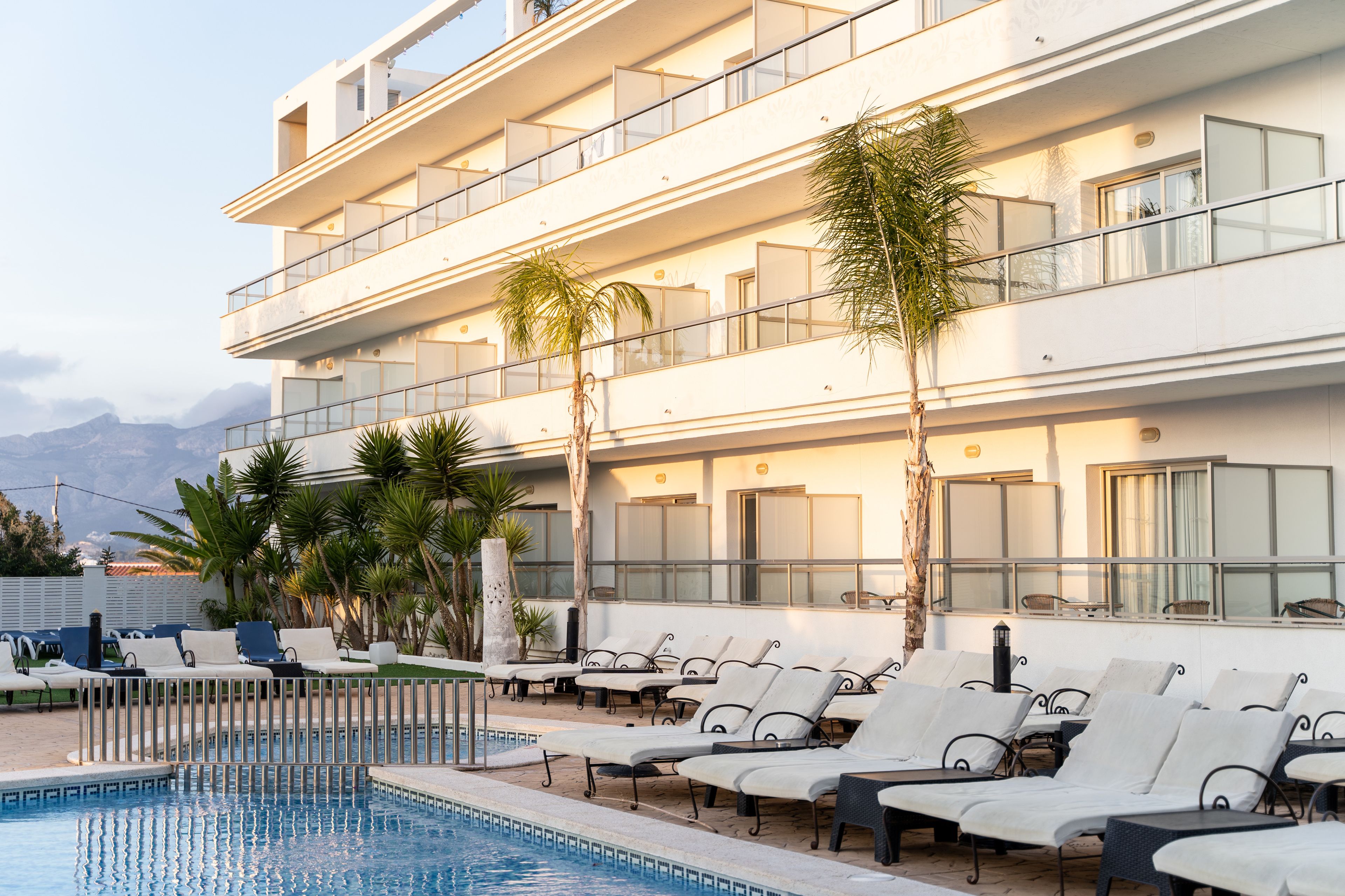 A modern hotel with a pool area, multiple balconies, and palm trees.