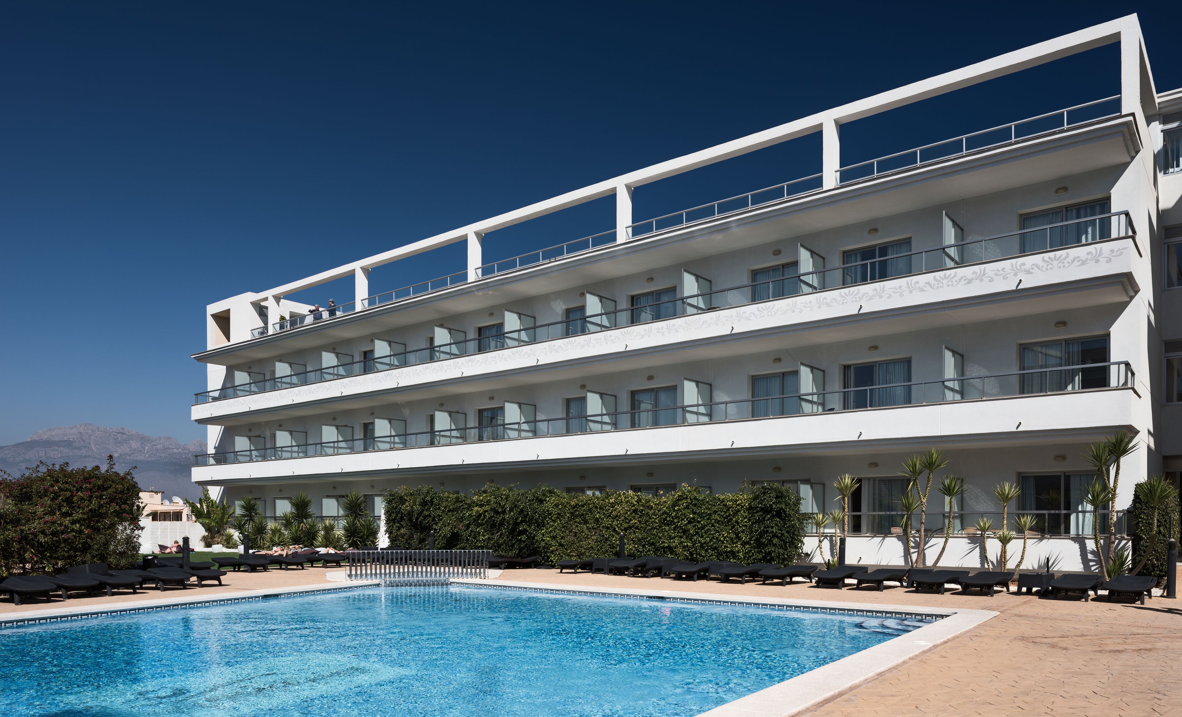 Ein mehrstöckiges Hotel mit Schwimmbad, Balkonen und Bergblick.