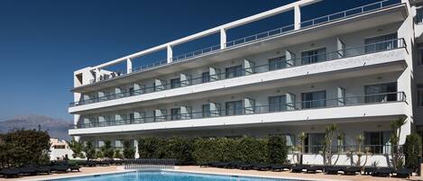 Un hotel de varios pisos con piscina, balcones y vistas a las montañas.