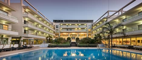 A multi-story hotel with a central pool, balconies, and a well-lit entrance.