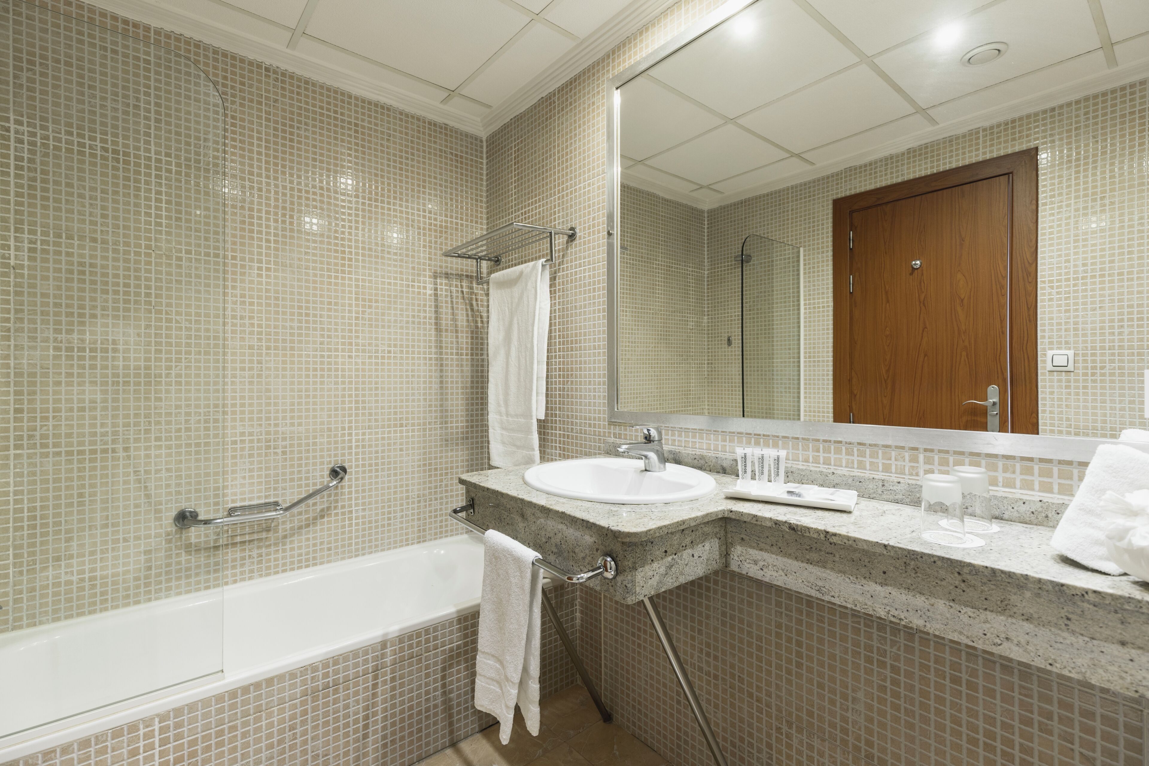 A bathroom with a bathtub, sink, mirror, and towel rack.