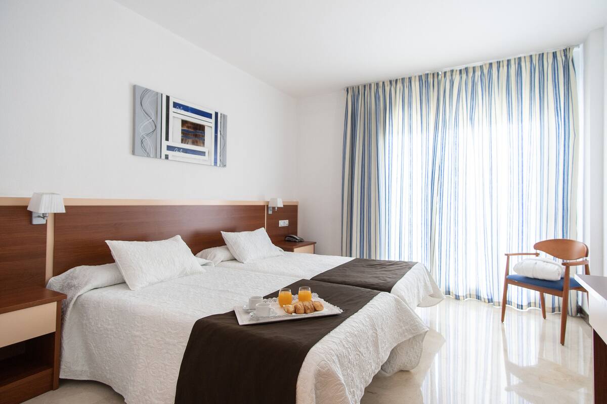 A hotel room with a large bed, a desk, a chair, a nightstand, and a tray with breakfast items.