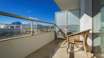 Ein Balkon mit Korbstühlen, einem Tisch und Blick auf Berge und Gebäude.